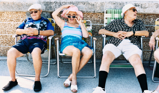 Senior Men and a Woman Sit on Deckchairs on the Pavement Sunbathing